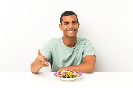 Young handsome man with salad in a table handshaking after good dealの写真素材