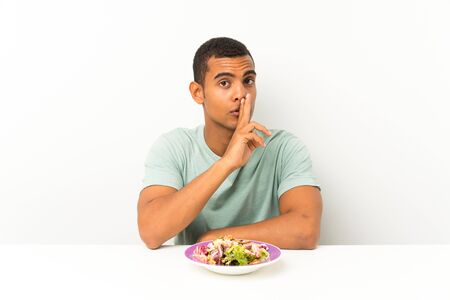 Young handsome man with salad in a table doing silence gestureの写真素材