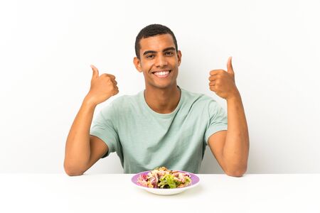 Young handsome man with salad in a table giving a thumbs up gestureの写真素材