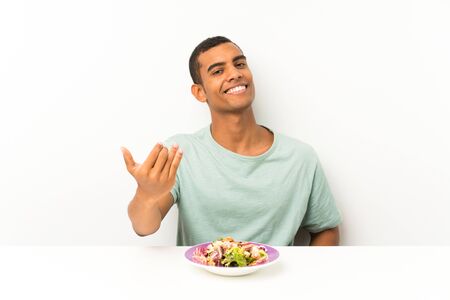 Young handsome man with salad in a table inviting to comeの写真素材