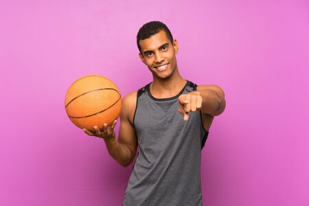 Young sport man with ball of basketball over isolated purple wall points finger at you with a confident expressionの写真素材