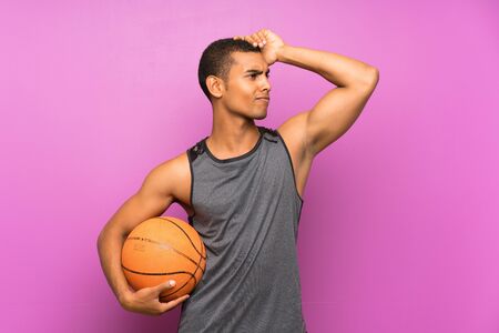 Young sport man with ball of basketball over isolated purple wall having doubts and with confuse face expressionの写真素材