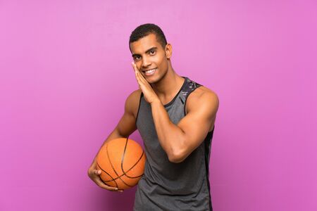 Young sport man with ball of basketball over isolated purple wall whispering somethingの写真素材