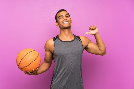 Young sport man with ball of basketball over isolated purple wall proud and self-satisfiedの写真素材