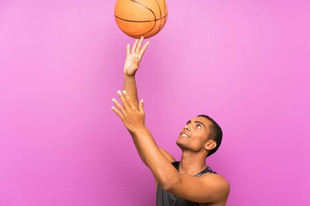 Young sport man with ball of basketball over isolated purple wallの写真素材