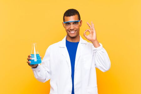 Scientific man holding a laboratory flask over isolated background showing ok sign with fingersの写真素材