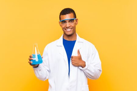 Scientific man holding a laboratory flask over isolated background with thumbs up because something good has happenedの写真素材
