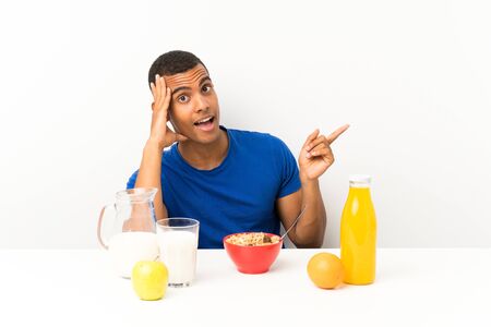 Young man having breakfast in a table surprised and pointing finger to the sideの写真素材