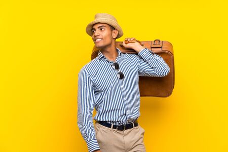 Brunette man holding a vintage briefcase over isolated yellow background looking sideの写真素材