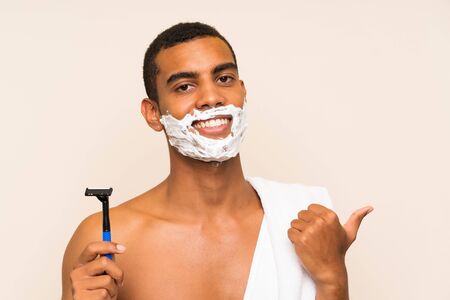 Young handsome man shaving his beard over isolated background pointing to the side to present a productの写真素材