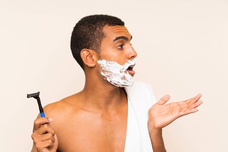 Young handsome man shaving his beard over isolated background with surprise facial expressionの写真素材