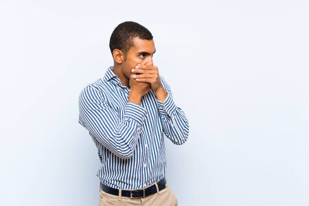 Young handsome brunette man over isolated blue background covering mouth and looking to the sideの写真素材