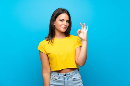 Young girl over isolated blue background showing ok sign with fingersの写真素材