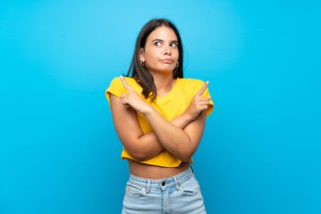 Young girl over isolated blue background pointing to the laterals having doubtsの写真素材