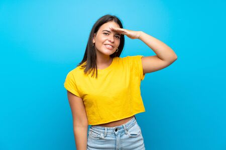 Young girl over isolated blue background looking far away with hand to look somethingの写真素材