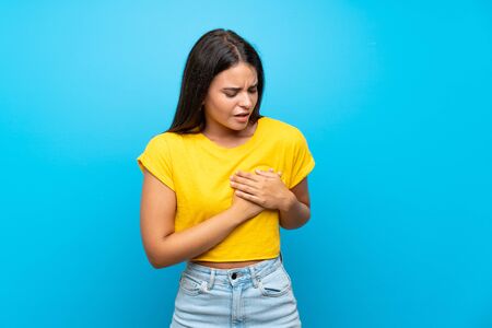 Young girl over isolated blue background having a pain in the heartの写真素材
