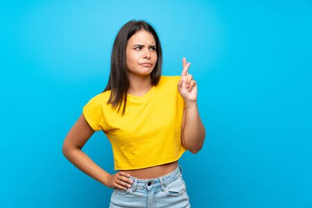 Young girl over isolated blue background with fingers crossing and wishing the bestの写真素材