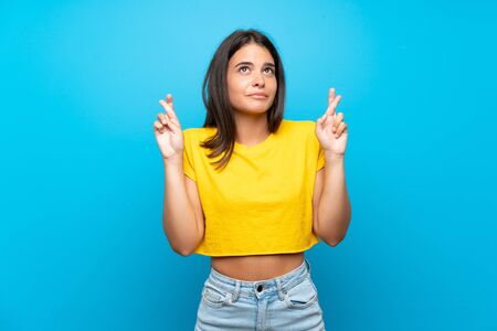 Young girl over isolated blue background with fingers crossing and wishing the bestの写真素材