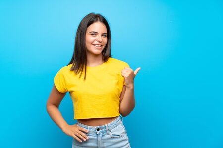 Young girl over isolated blue background pointing to the side to present a productの写真素材