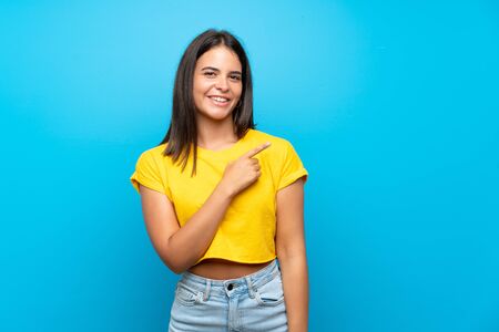 Young girl over isolated blue background pointing to the side to present a productの写真素材