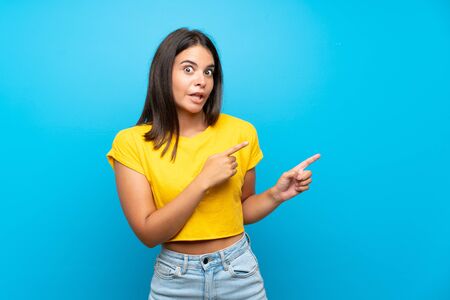 Young girl over isolated blue background frightened and pointing to the sideの写真素材