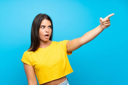 Young girl over isolated blue background pointing awayの写真素材