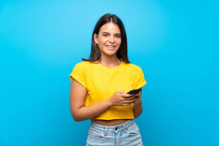 Young girl over isolated blue background sending a message with the mobileの写真素材