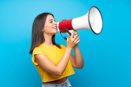 Young girl over isolated blue background shouting through a megaphoneの写真素材