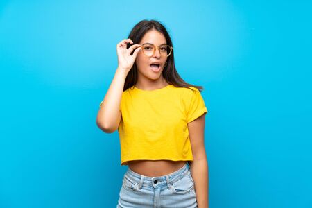 Young girl over isolated blue background with glasses and surprisedの写真素材