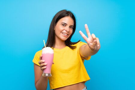 Young girl with strawberry milkshake over isolated background smiling and showing victory signの写真素材