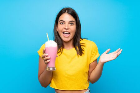 Young girl with strawberry milkshake over isolated background with shocked facial expressionの写真素材