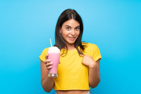 Young girl with strawberry milkshake over isolated background with surprise facial expressionの写真素材