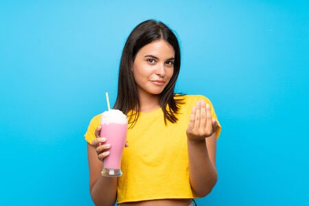 Young girl with strawberry milkshake over isolated background inviting to come with hand. Happy that you cameの写真素材