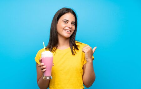 Young girl with strawberry milkshake over isolated background pointing to the side to present a productの写真素材