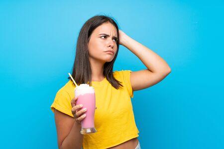 Young girl with strawberry milkshake over isolated background having doubts and with confuse face expressionの写真素材