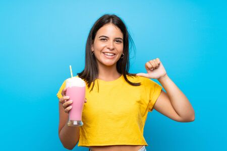 Young girl with strawberry milkshake over isolated background proud and self-satisfiedの写真素材