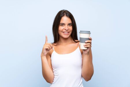 Young woman holding a take away coffee over isolated blue background pointing up a great ideaの写真素材