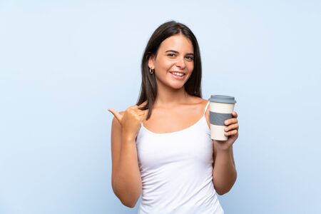 Young woman holding a take away coffee over isolated blue background pointing to the side to present a productの写真素材