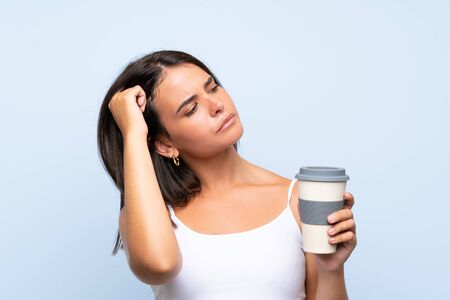 Young woman holding a take away coffee over isolated blue background having doubts and with confuse face expressionの写真素材