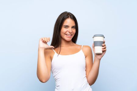Young woman holding a take away coffee over isolated blue background proud and self-satisfiedの写真素材