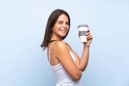 Young woman holding a take away coffee over isolated blue backgroundの写真素材