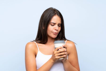 Young woman holding a take away coffee over isolated blue backgroundの写真素材