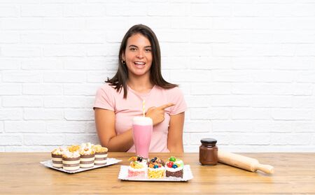Young girl with lots of different mini cakes pointing finger to the sideの写真素材