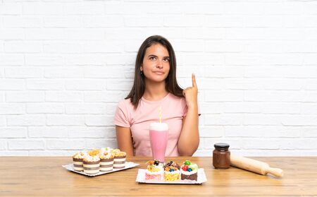 Young girl with lots of different mini cakes pointing with the index finger a great ideaの写真素材