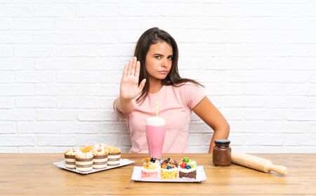 Young girl with lots of different mini cakes making stop gesture with her handの写真素材