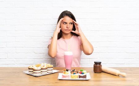 Young girl with lots of different mini cakes unhappy and frustrated with something. Negative facial expressionの写真素材