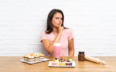 Young girl with lots of different mini cakes doing silence gestureの写真素材