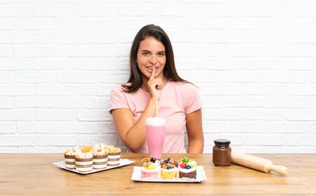 Young girl with lots of different mini cakes doing silence gestureの写真素材