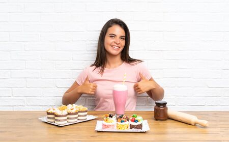 Young girl with lots of different mini cakes giving a thumbs up gestureの写真素材