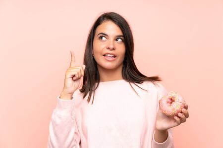 Young girl holding a donut over isolated pink background intending to realizes the solution while lifting a finger upの写真素材